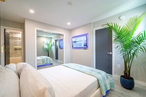 Una habitación de hotel moderna con una cama grande, un televisor, una planta en maceta y una zona de ducha.