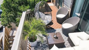 Un balcon agrémenté de meubles en osier, d’une plante en pot et d’une table à carreaux.