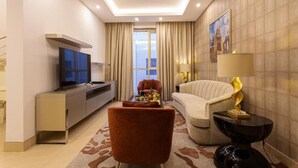 Ein modernes Hotelzimmer mit Flachbildfernseher, einer Couch, einem Sessel, einem Couchtisch und einer Lampe.