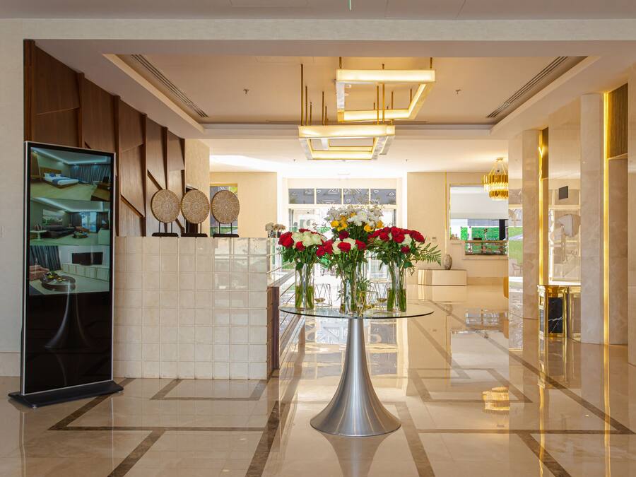 Um lobby moderno com uma mesa de vidro, um monitor digital e um arranjo floral.