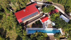 Vista aérea de una propiedad con un edificio de techo rojo, piscina y follaje circundante.
