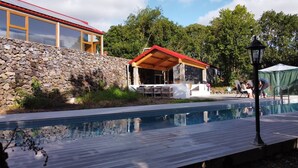 Una piscina con un muro de piedra y una zona de estar cubierta.