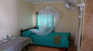 Una habitación pequeña con una cama, una mesa y un ventilador.