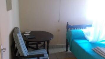 Quarto com cama, cadeira, mesa pequena e janela.