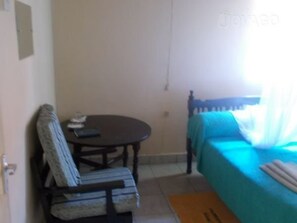 Una habitación con una cama, una silla, una mesita y una ventana.