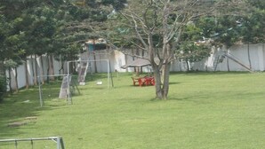 Un patio con césped, un árbol, un pequeño refugio y una silla roja.