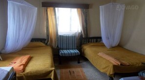 Una habitación con dos camas individuales, una silla y un ventanal con cortinas.
