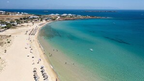 Una playa costera con aguas claras, una orilla arenosa y algunos edificios al fondo.