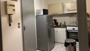 A compact kitchen with a refrigerator, microwave, and stove. There is a trash bin and a hanging light fixture. - L'Appart 1 des Thermes (Rochefort)