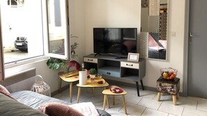 A living room with a TV, a small table with a plant and a candle, a sofa, and a door. - L'Appart 1 des Thermes (Rochefort)