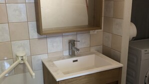 A bathroom with a white sink, wooden cabinet, and a mirror. - L'Appart 1 des Thermes (Rochefort)