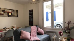 A modern living room with a grey sofa, a dining table with breakfast items, a blackboard with French phrases, and a window with a view of the street. - L'Appart 1 des Thermes (Rochefort)