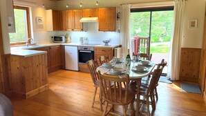 Une cuisine spacieuse avec des meubles en bois, un coin repas avec une table pour quatre personnes et une vue sur l’extérieur grâce à une porte-fenêtre coulissante.