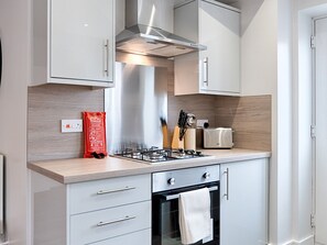 Une cuisine moderne équipée d’une cuisinière à gaz, d’un four et d’un grille-pain. On peut voir une couverture anti-feu posée sur le plan de travail, ainsi qu’un bloc à couteaux.