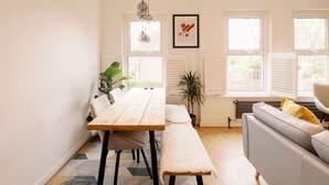 A modern dining area with a wooden table, bench, and pendant lights. There is a sofa with cushions and a potted plant. - Lush Retreat with Garden - Pass the Keys (London)