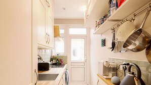 A narrow kitchen with white cabinets, a toaster, a kettle, and a window. - Lush Retreat with Garden - Pass the Keys (London)