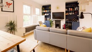A modern living room with a sofa, a TV, and a bookshelf. - Lush Retreat with Garden - Pass the Keys (London)
