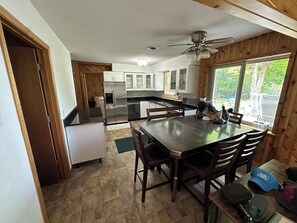 Una cucina con zona pranzo, pareti in legno, una ventola a soffitto e vista sull'esterno.