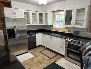 Una cucina moderna con mobili bianchi, elettrodomestici in acciaio inossidabile e un piano di lavoro nero.