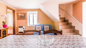 Ein Essbereich mit einem Tisch für zwei Personen, einem blauen Sofa, einer Treppe und einem Fenster mit Vorhängen.