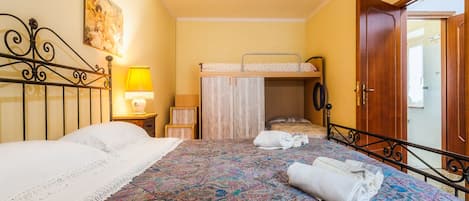 A bedroom with a bunk bed, a bedside table with a lamp, and a door leading to another room.