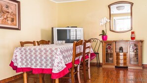 Ein Essbereich mit einem für vier Personen gedeckten Tisch, einem Fernseher, einer Kommode mit Dekoration und einem gerahmten Bild an der Wand.