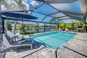 A swimming pool with lounge chairs and umbrellas, surrounded by a covered patio area.