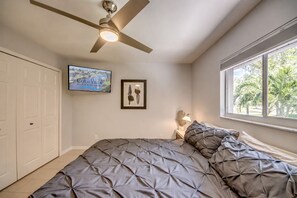 Ein Schlafzimmer mit Bett, Deckenventilator, Fenster mit Blick und einem gerahmten Bild an der Wand.