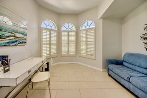 A room with a desk, a chair, a blue sofa, and three bay windows with shutters. - Villa 4Friends, modern, preferred location, heated pool, south facing (Cape Coral)