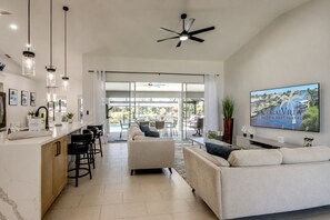 A modern living room with a sofa, a TV mounted on the wall, and a bar area with stools. - Villa 4Friends, modern, preferred location, heated pool, south facing (Cape Coral)