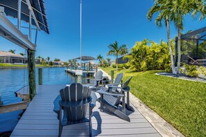 Ein Deck am Wasser mit Adirondack-Stühlen und einem Tisch, mit Blick auf einen Yachthafen, Boote und einen wolkenlosen, blauen Himmel.