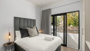 Un dormitorio moderno con una cama grande, una mesita de noche con lámpara y vistas al exterior a través de un ventanal corredero.