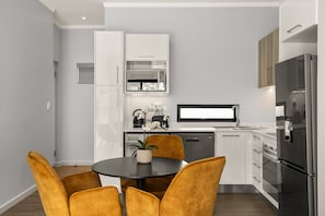 Eine moderne Küche mit weißen Schränken, einem schwarzen Kühlschrank und einem Essbereich mit einem runden Tisch und gelben Stühlen.