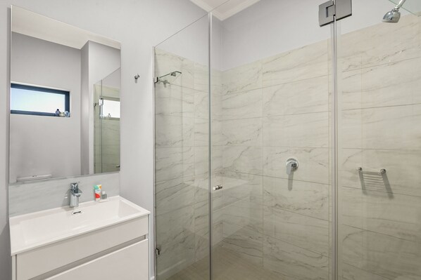 Un baño moderno con cabina de ducha de vidrio, un lavabo blanco con espejo y una pequeña ventana sobre el lavabo.