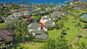 An aerial view of a residential area with houses, palm trees, and a view of the ocean. - Manualoha 903 Steps to Poipu Beach (Koloa)