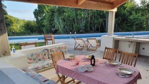 An outdoor dining area with a table set for two, surrounded by wooden chairs and a cushioned bench. - Domes Azalia (Angra do Heroísmo)