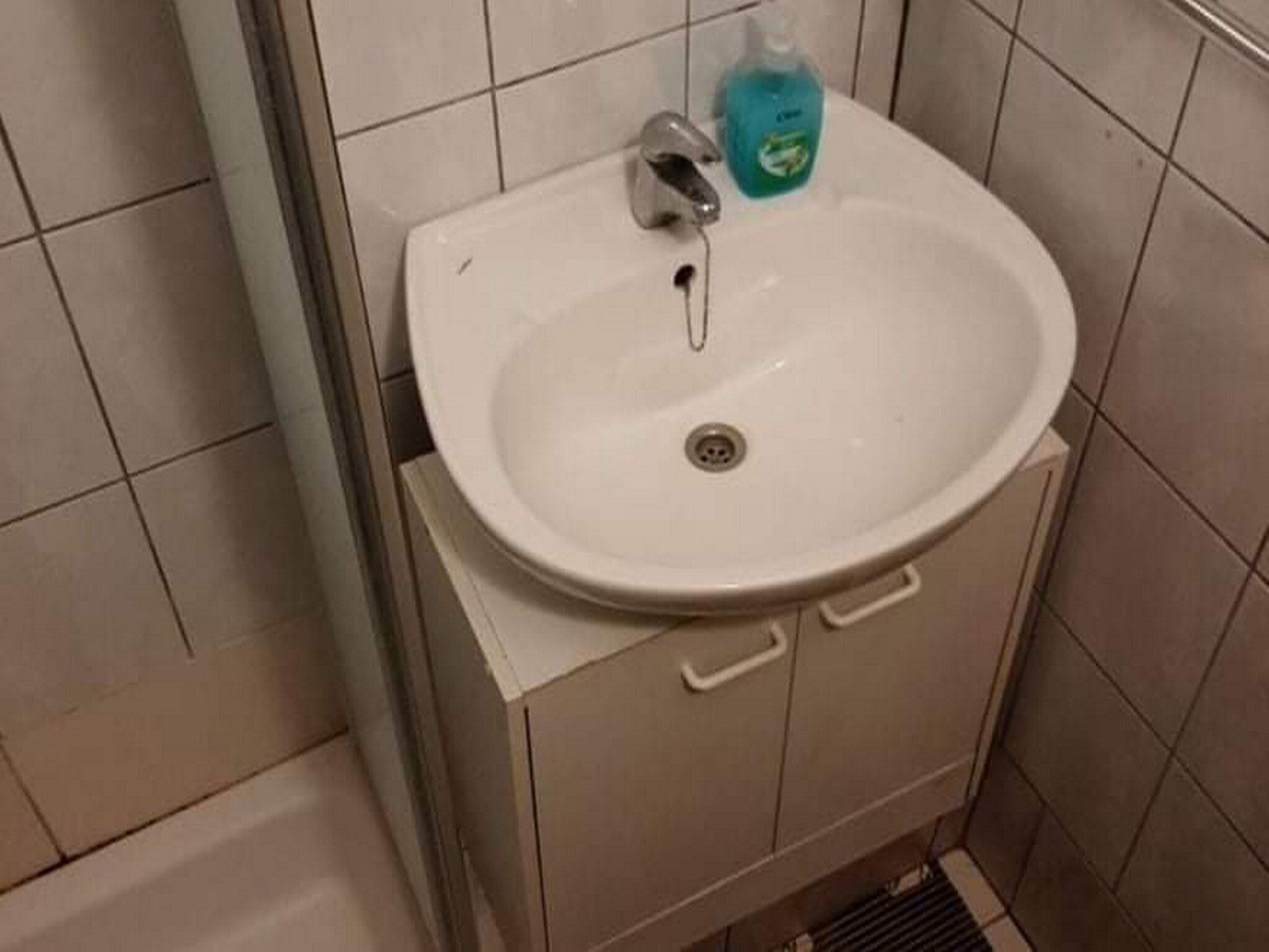 A bathroom with a white sink, a faucet, and a soap dispenser.