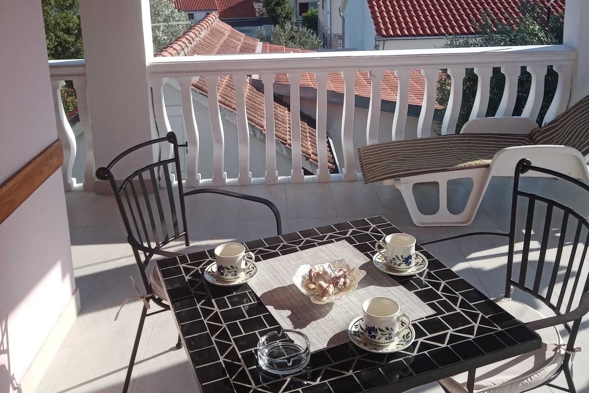 Ein Balkon mit Tisch für zwei Personen, Stühlen und Blick auf Gebäude mit roten Ziegeln sowie Grünflächen.