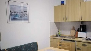 A compact kitchen with a dining area, a single chair, a small table, and a sofa. - Apartments Marija (Pirovac)