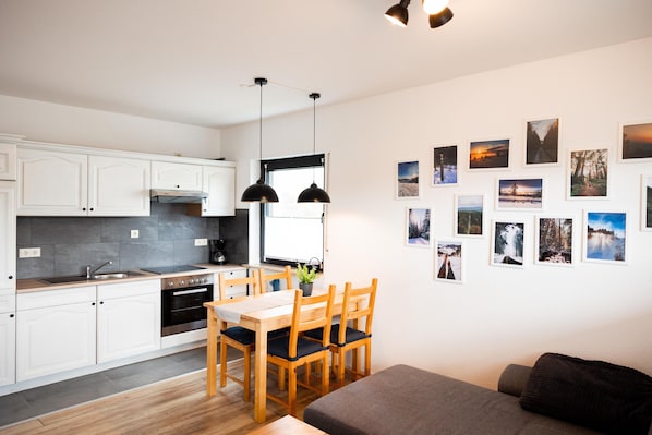 A modern kitchen with white cabinets, a wooden dining table, and black pendant lights.