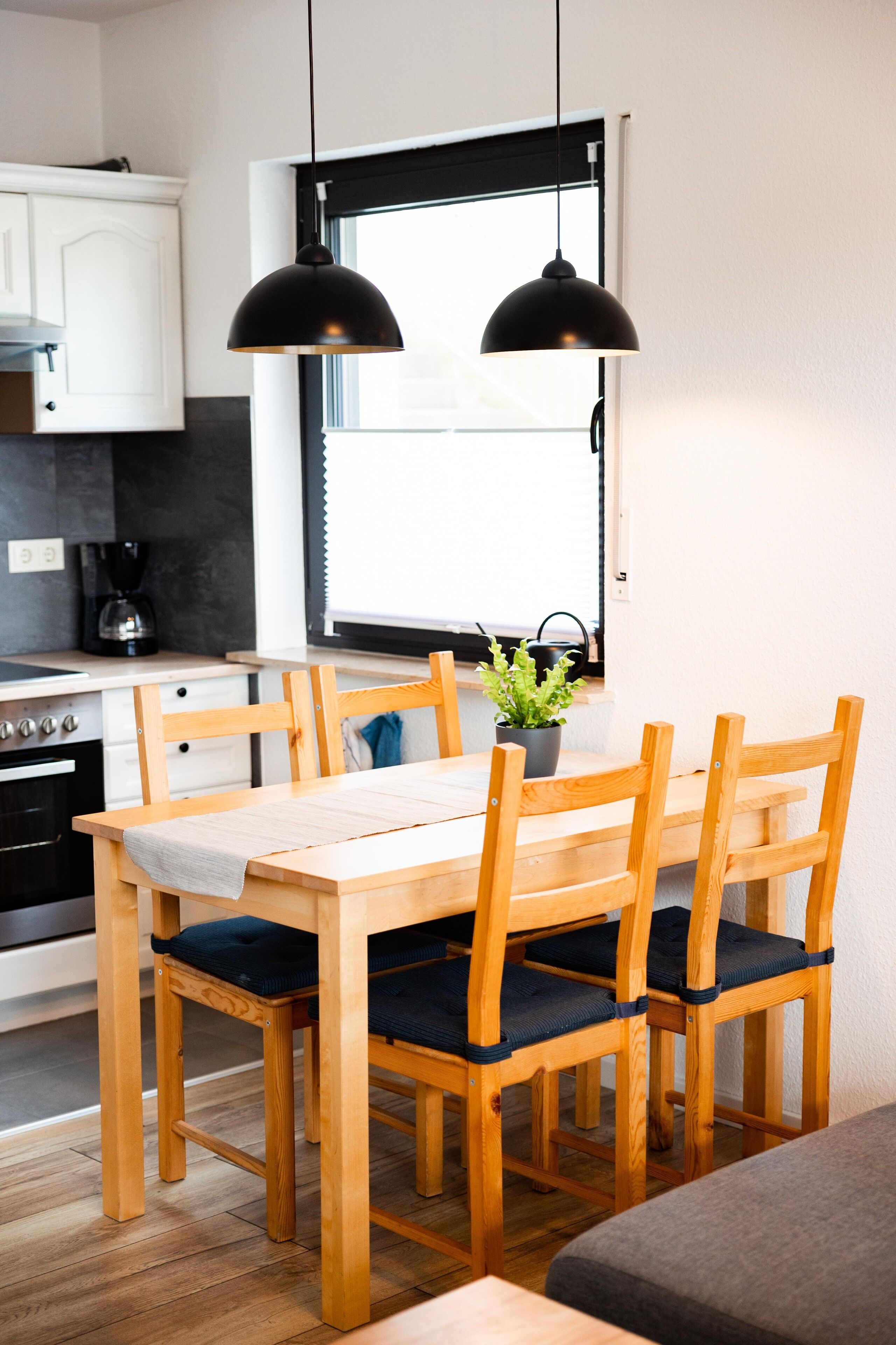 A kitchen with a wooden table and chairs, a coffee maker, and a window with blinds.