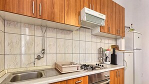 A kitchen with wooden cabinets, a stainless steel sink, a gas stove, an oven, and a refrigerator. - Apartment Lucija (Kastela)