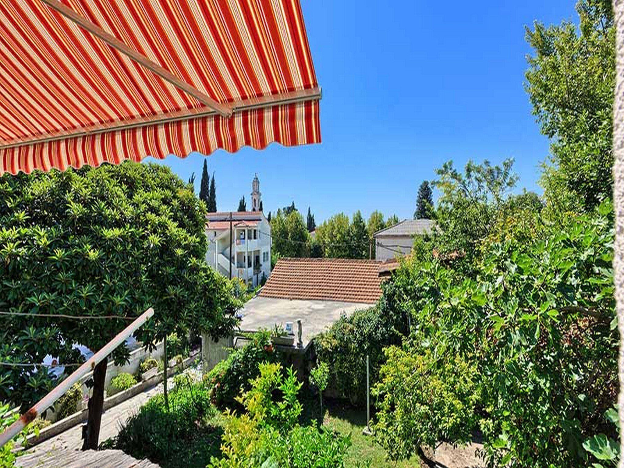 A courtyard with a red striped awning, a white building with a red roof, and lush greenery.