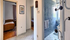 A hotel room with a bed, a bathroom with a shower, and a hallway leading to another room. - Apartment Lucija (Kastela)