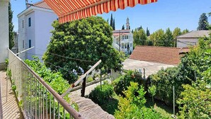 A balcony with a red striped awning overlooking a garden and buildings. - Apartment Lucija (Kastela)