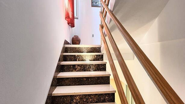 A staircase with alternating dark and light steps, a wooden handrail, and a vase on the landing. - Apartment Lucija (Kastela)
