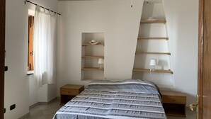 A bedroom with a bed, a wooden nightstand, a shelf unit, and a window with curtains.