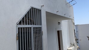 A white building with a barred window, a door, and a small balcony with a metal railing.