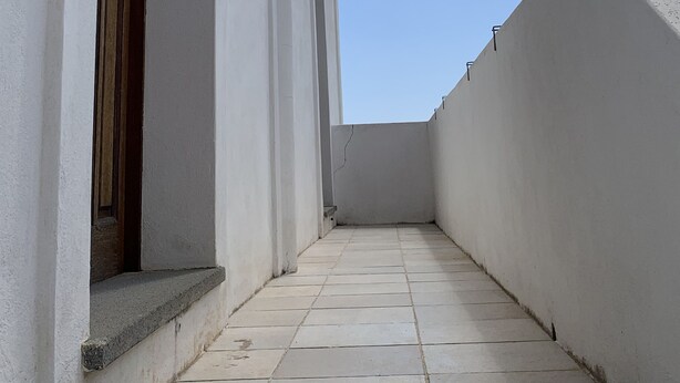 A narrow corridor with a tiled floor, a wooden door, and a white wall with a small window.