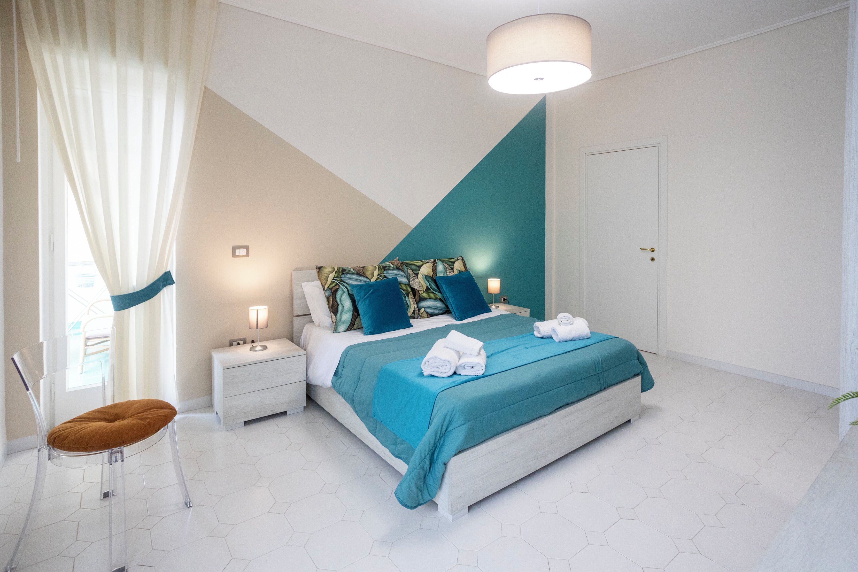 A modern bedroom with a bed, nightstands, a chair, and a window with curtains.